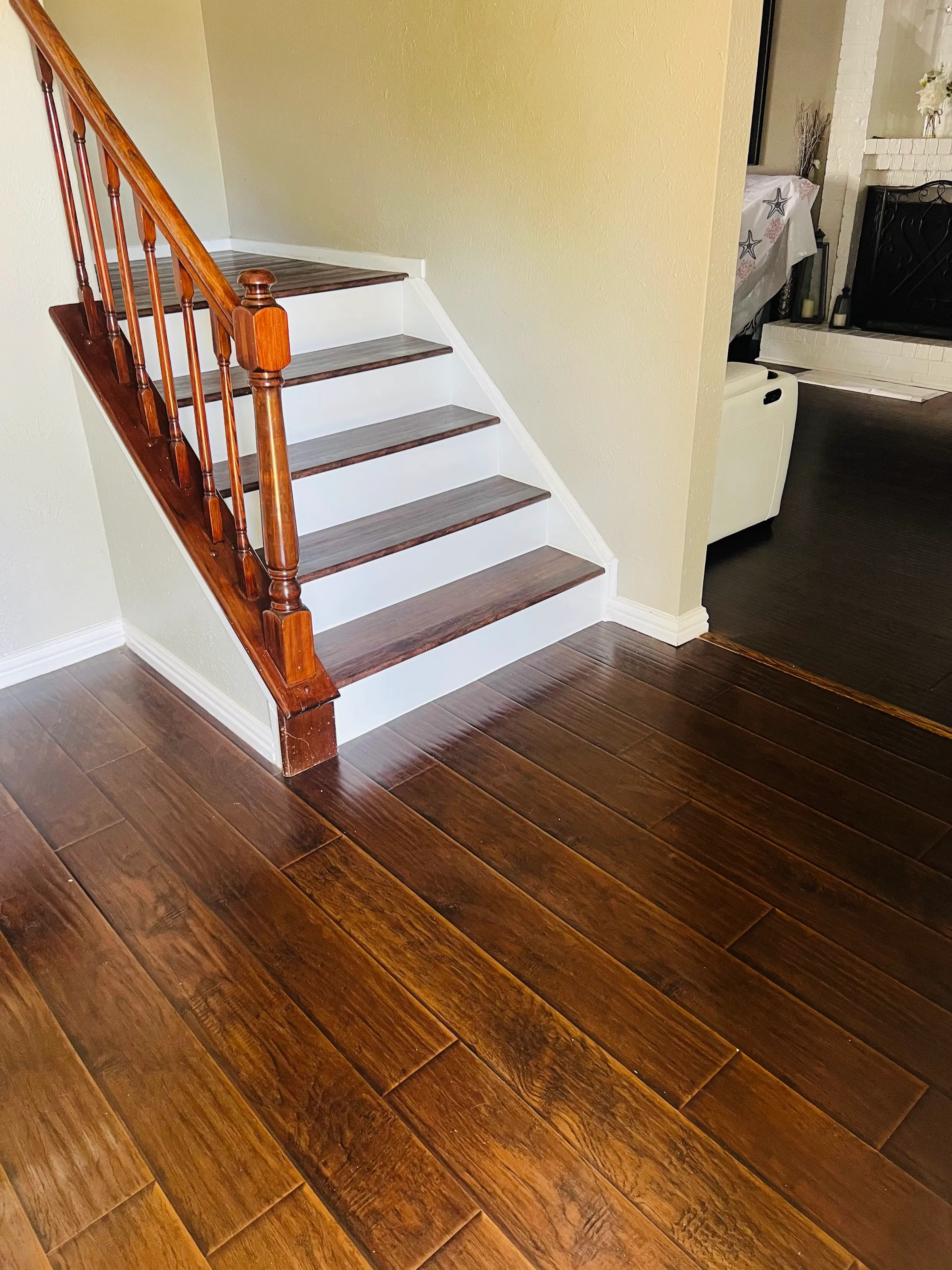 Vista del nuevo piso vinílico de lujo (LVP) con apariencia de madera oscura en un descanso que lleva a escaleras con contrahuellas blancas y huellas de LVP, con un barandal de madera.