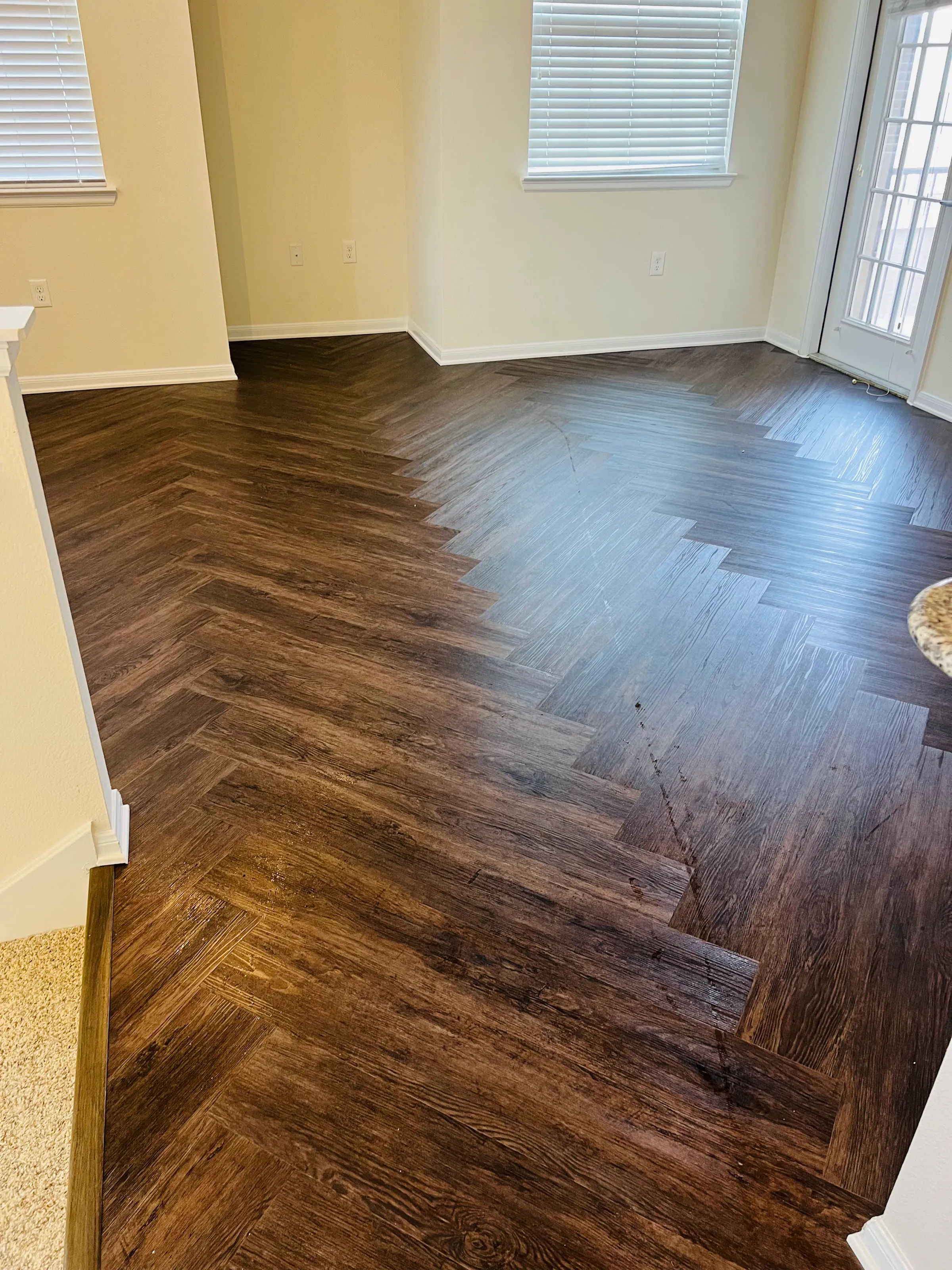 View of new dark LVP flooring in herringbone pattern leading to light carpeted stairs.