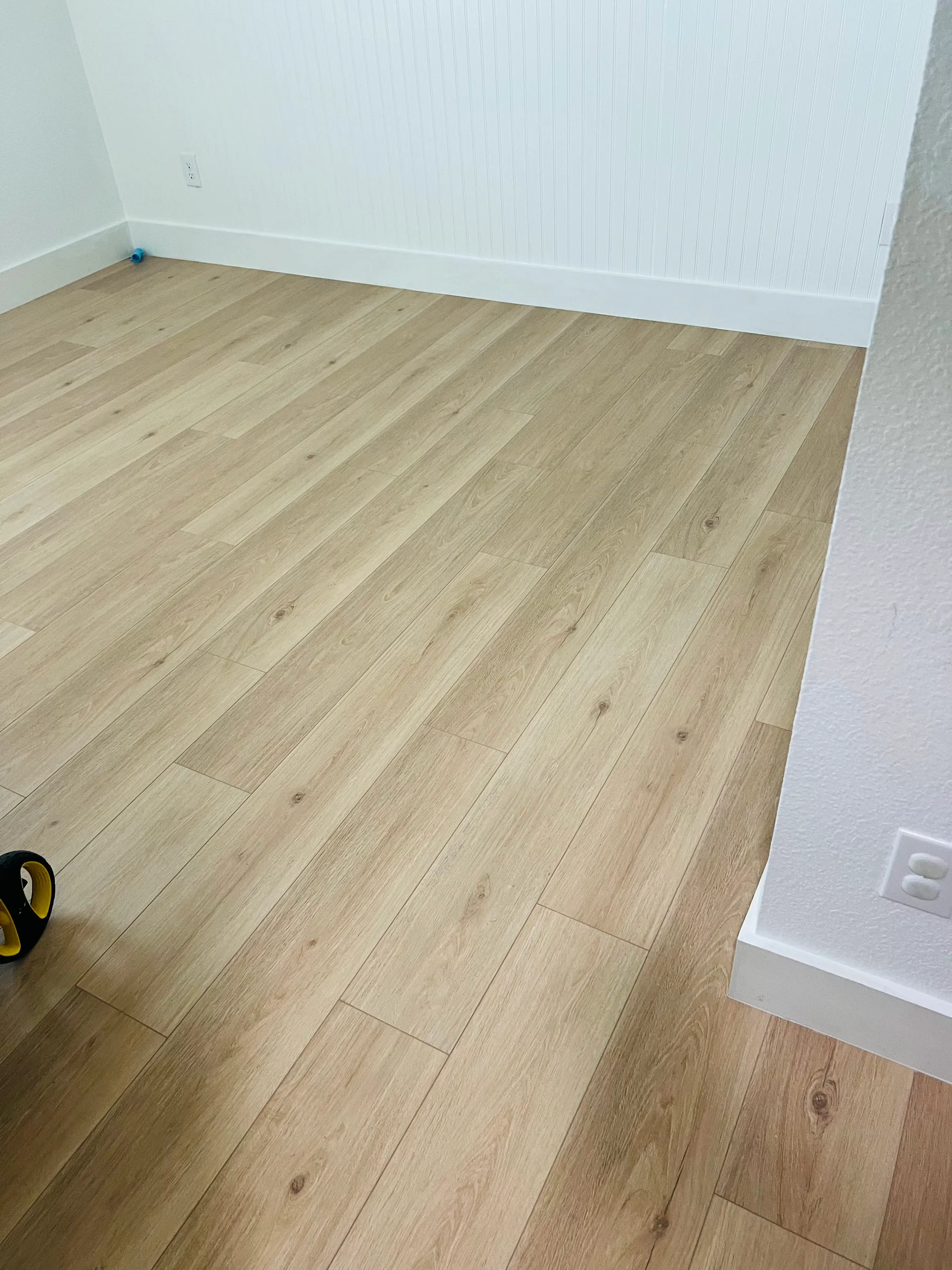 Vista general de una recámara con piso LVP de veta de madera clara recién instalado y zoclos blancos.