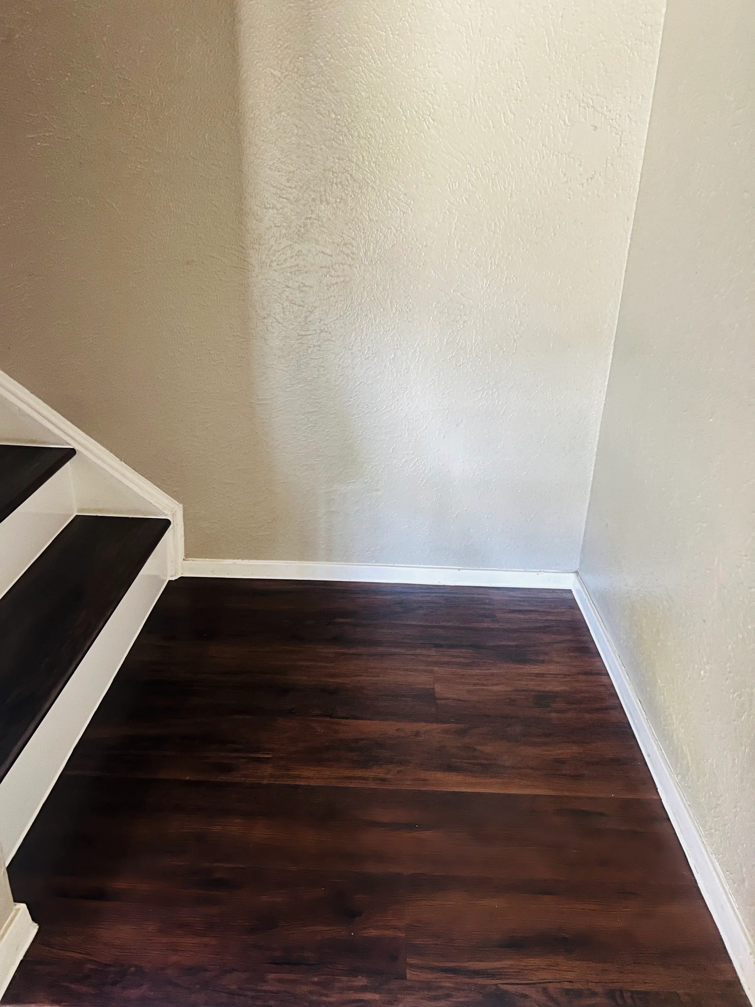 Primer plano del piso vinílico de lujo (LVP) con apariencia de madera oscura instalado en un descanso, con zoclos y paredes blancas.