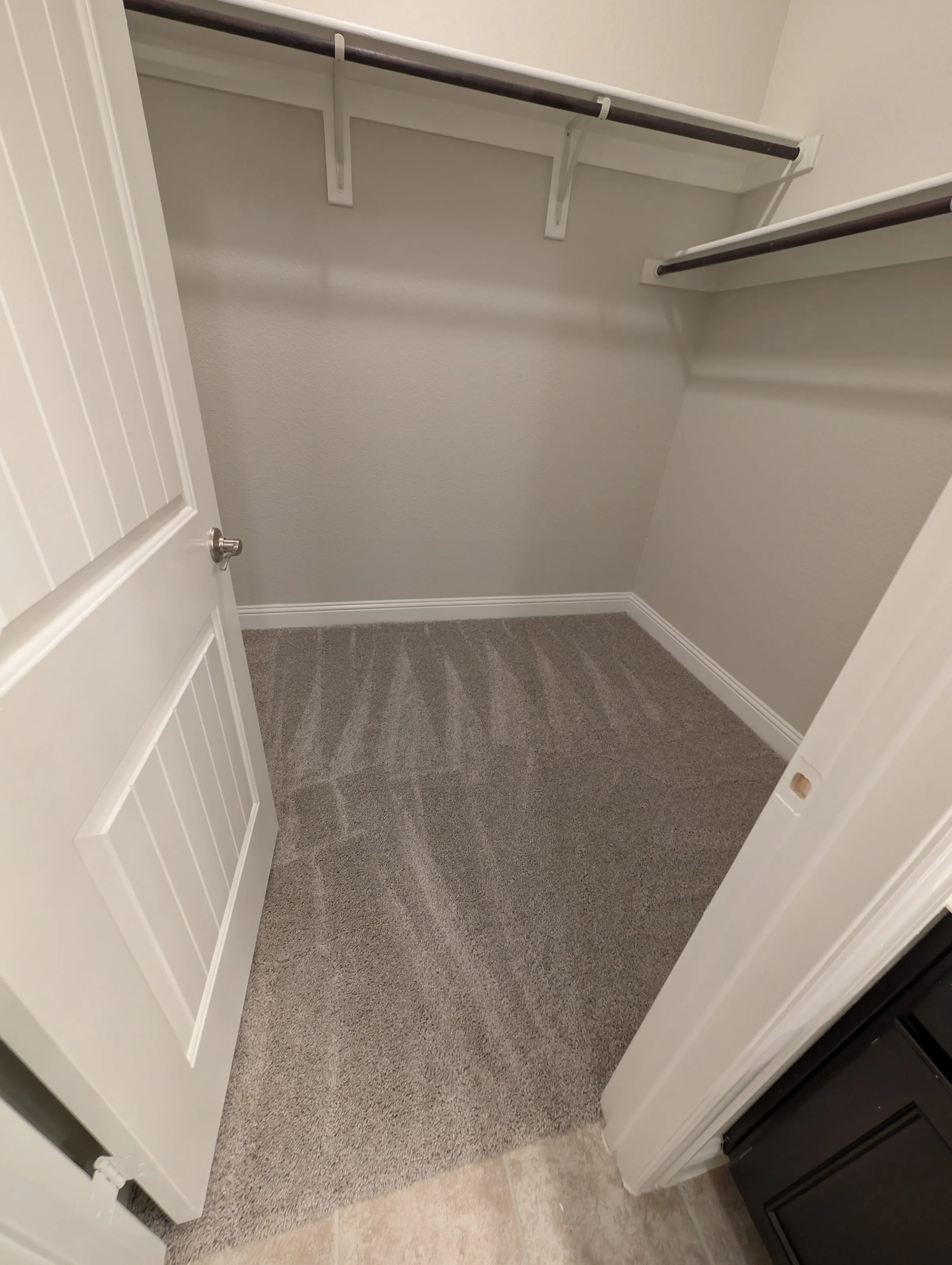 Interior de un clóset con alfombra gris texturizada nueva, estanterías blancas y el piso más claro del pasillo visible tras la puerta.
