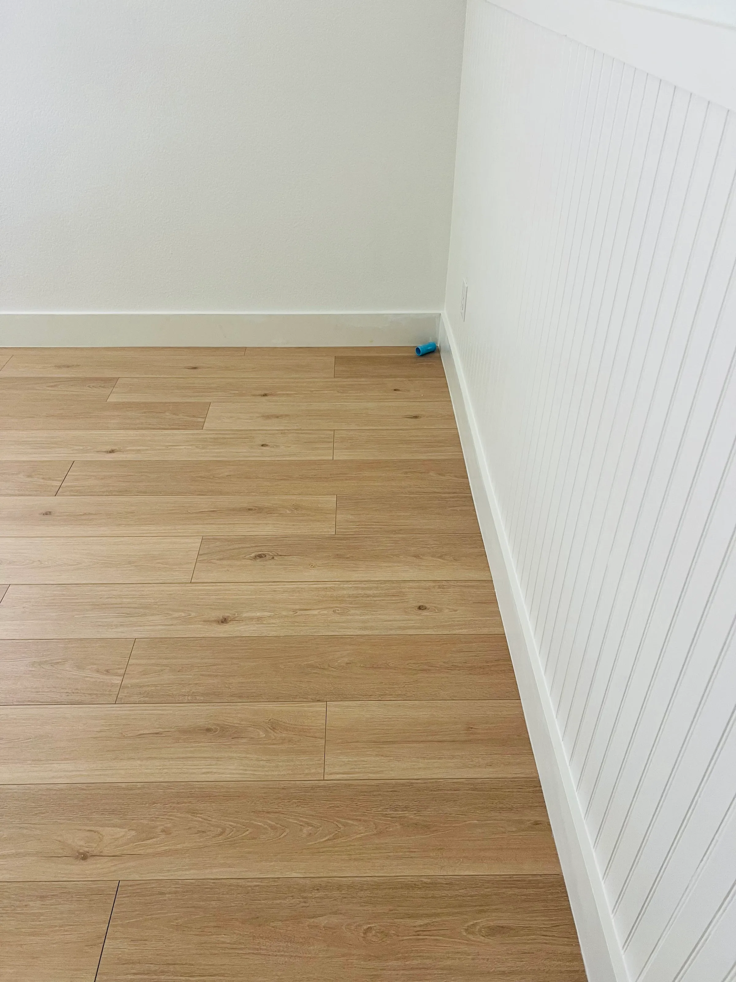 Primer plano de las tablas de piso LVP claro colocadas contra una pared de machihembrado blanco y zoclo.
