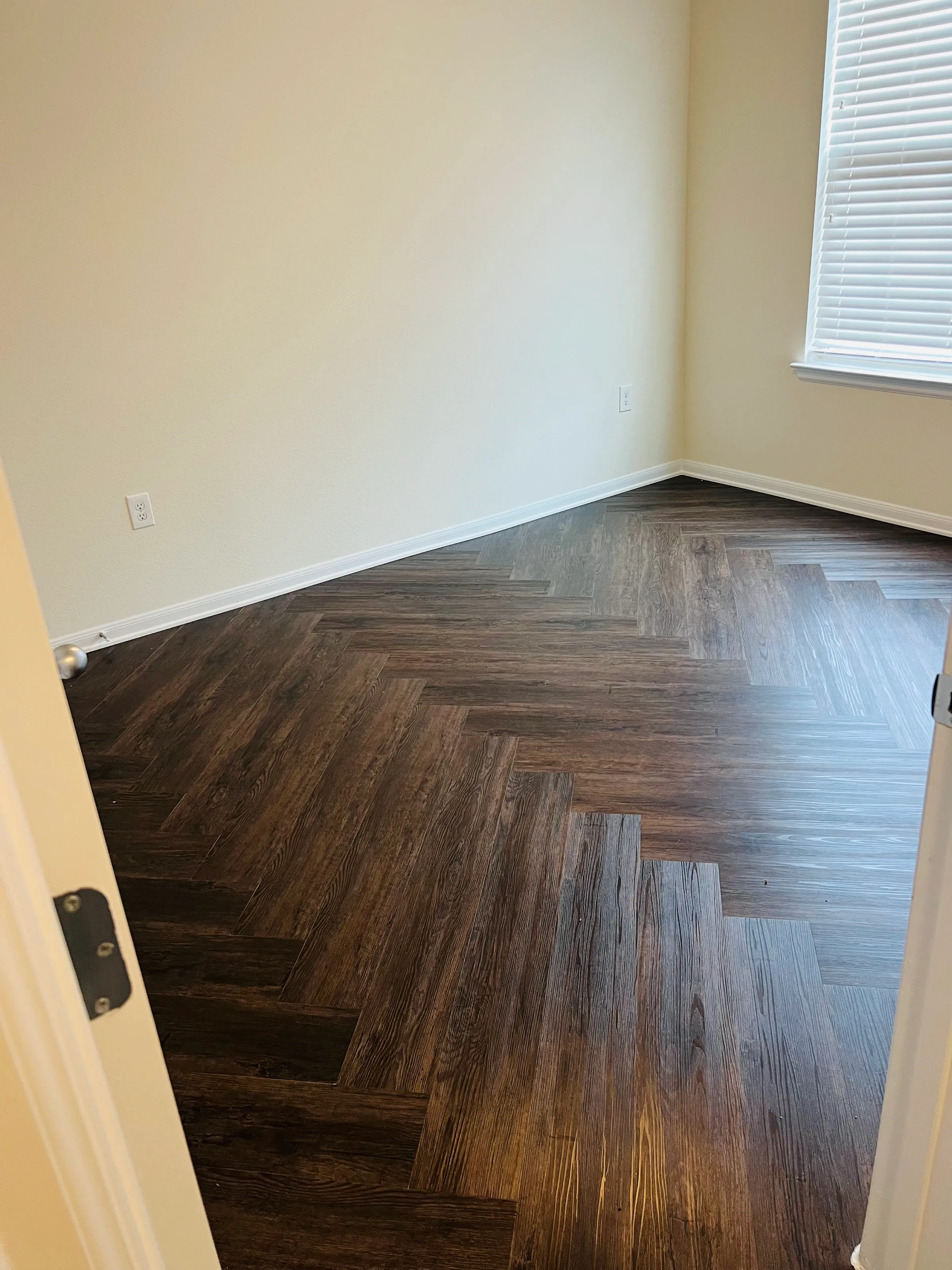 Close-up of new dark LVP herringbone flooring in a room with white baseboards and a window.