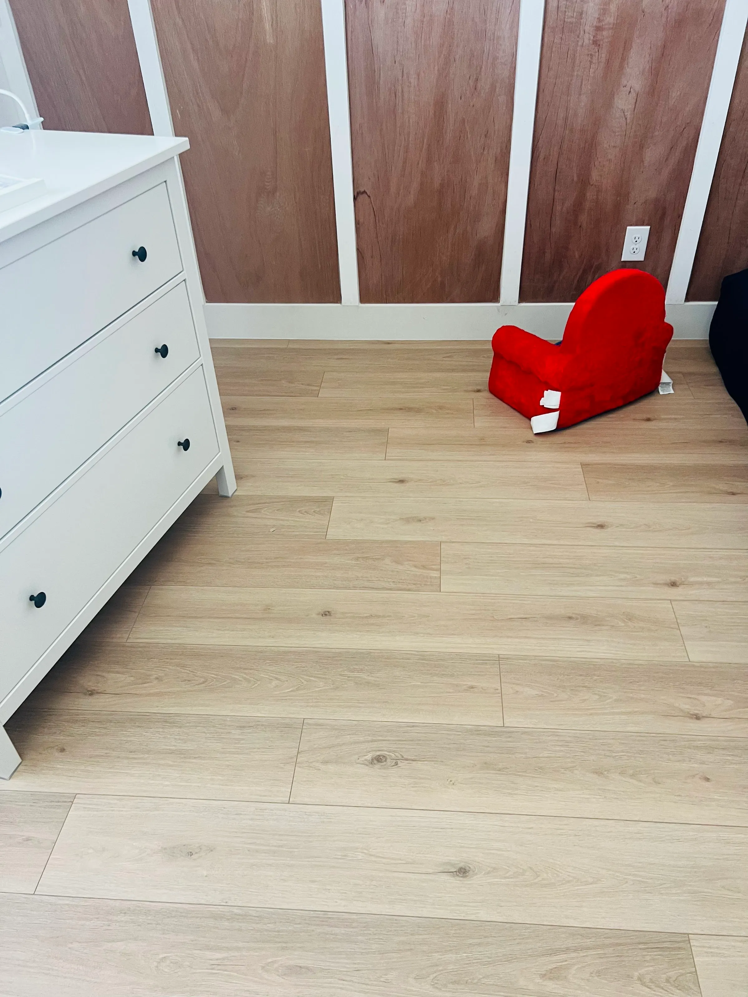 Piso LVP claro extendiéndose en una recámara con una cómoda blanca y una silla roja para niños.