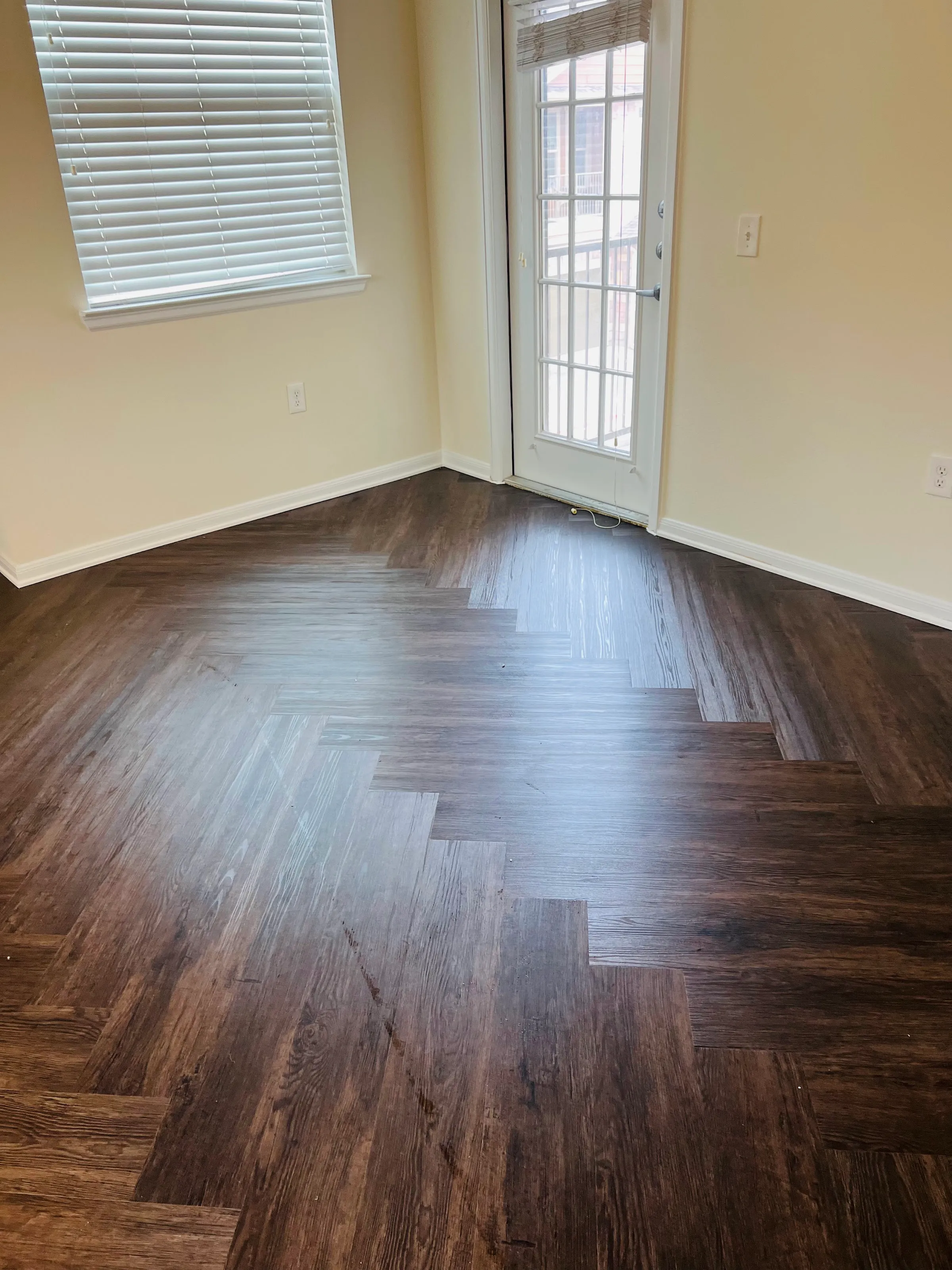 New dark LVP herringbone flooring in a room with a window and a glass-paneled door.
