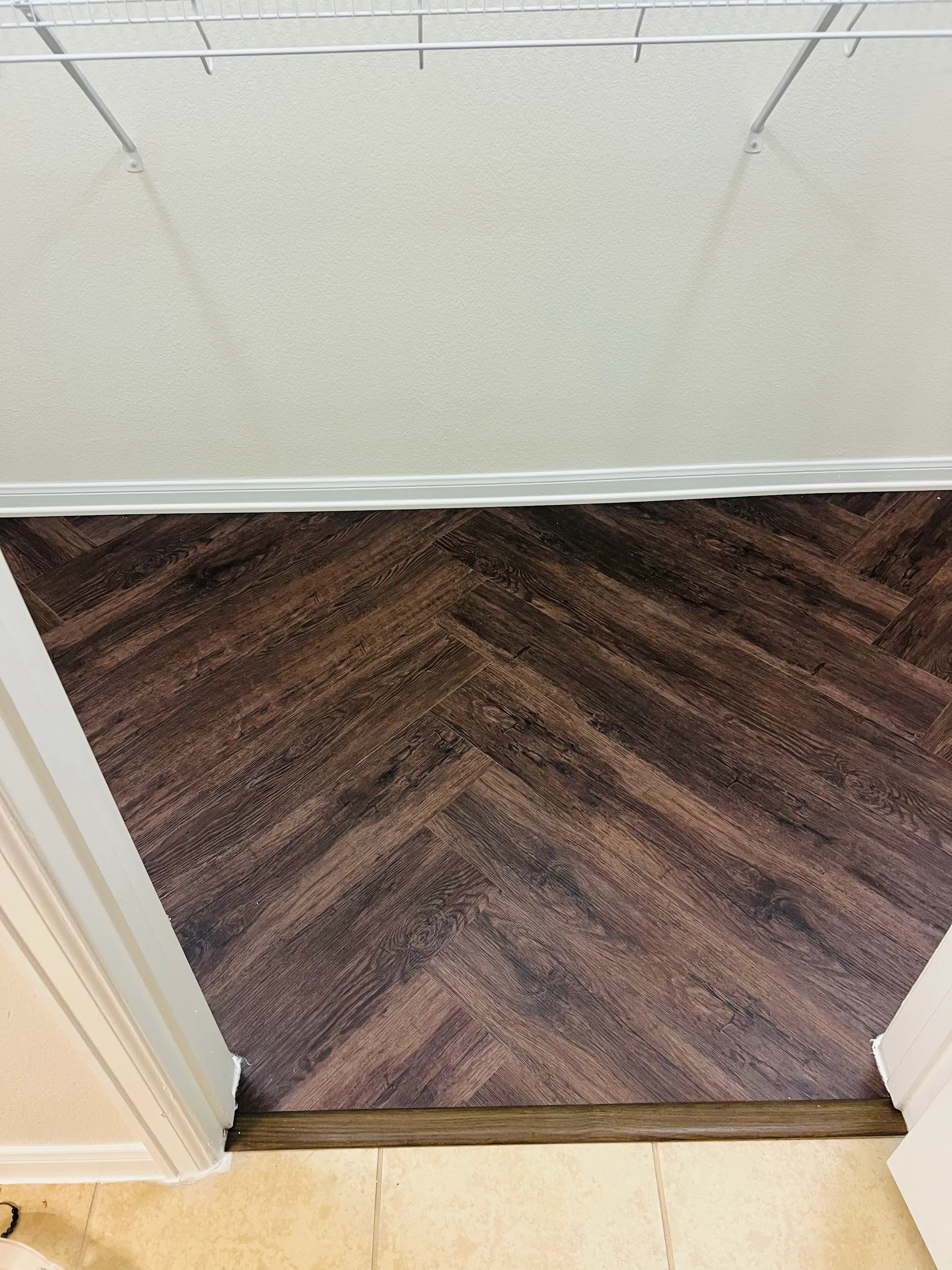Closet floor in the same dark herringbone LVP, with a transition strip at the tile.