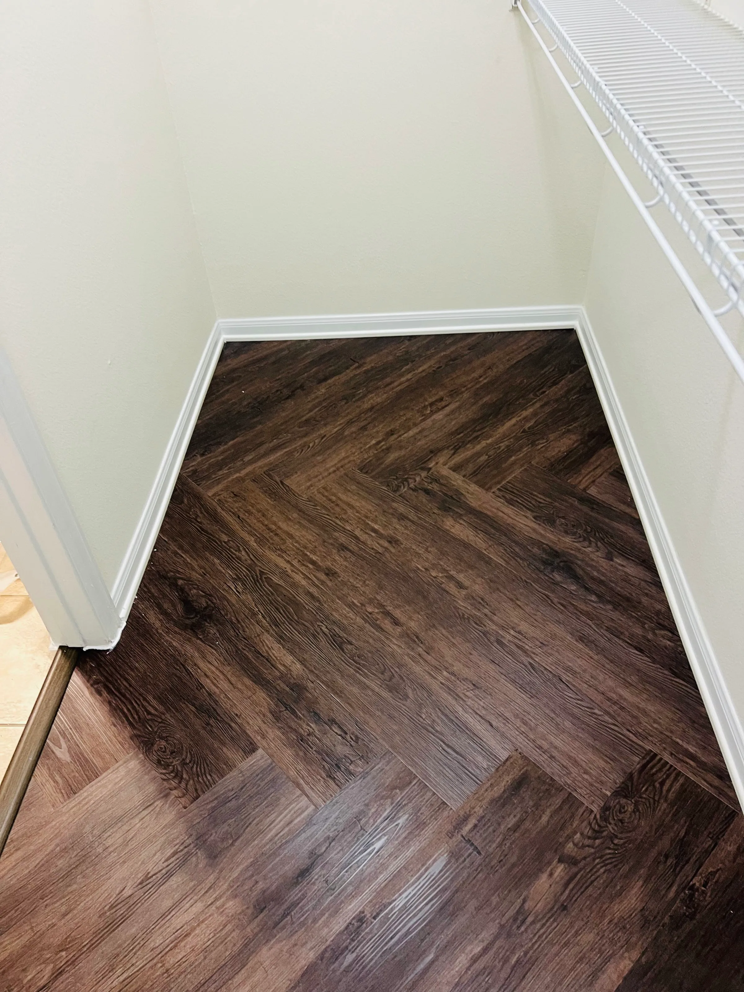 Herringbone LVP carried into a closet with white baseboards and wire shelving.